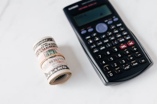 From above of modern electronic calculator with small display and buttons of different colors near roll of dollar bills on marble surface